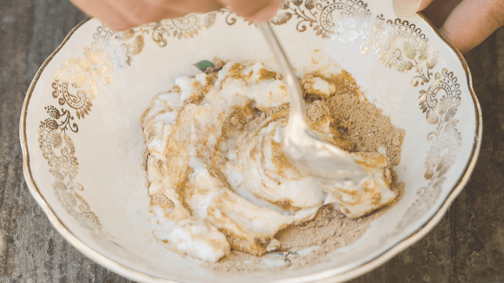 Mélange de crème blanche et poudre beige dans un bol décoratif blanc et doré tenu par des mains